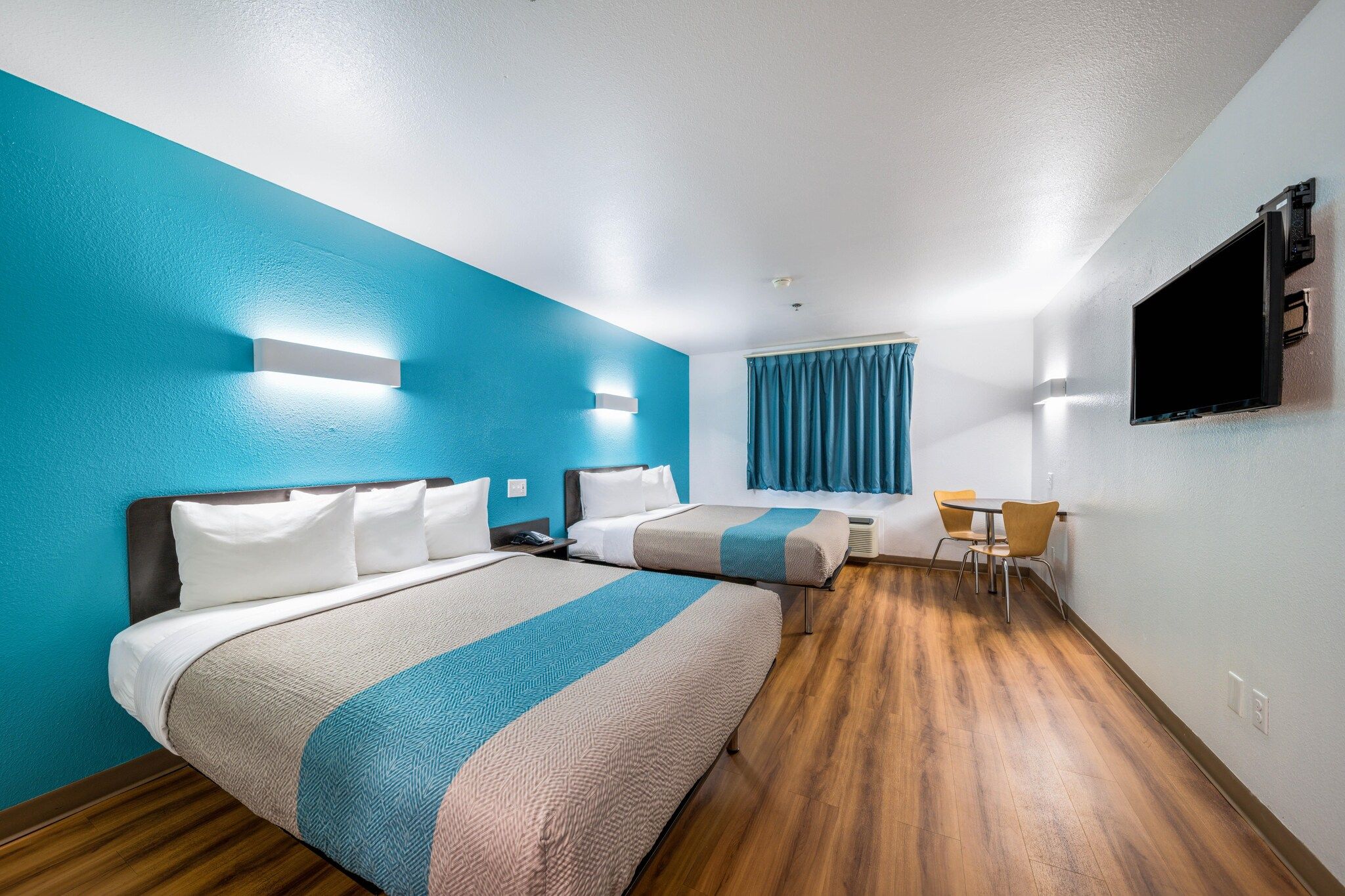 A hotel room with two beds, a desk, a chair, and a television on the wall.