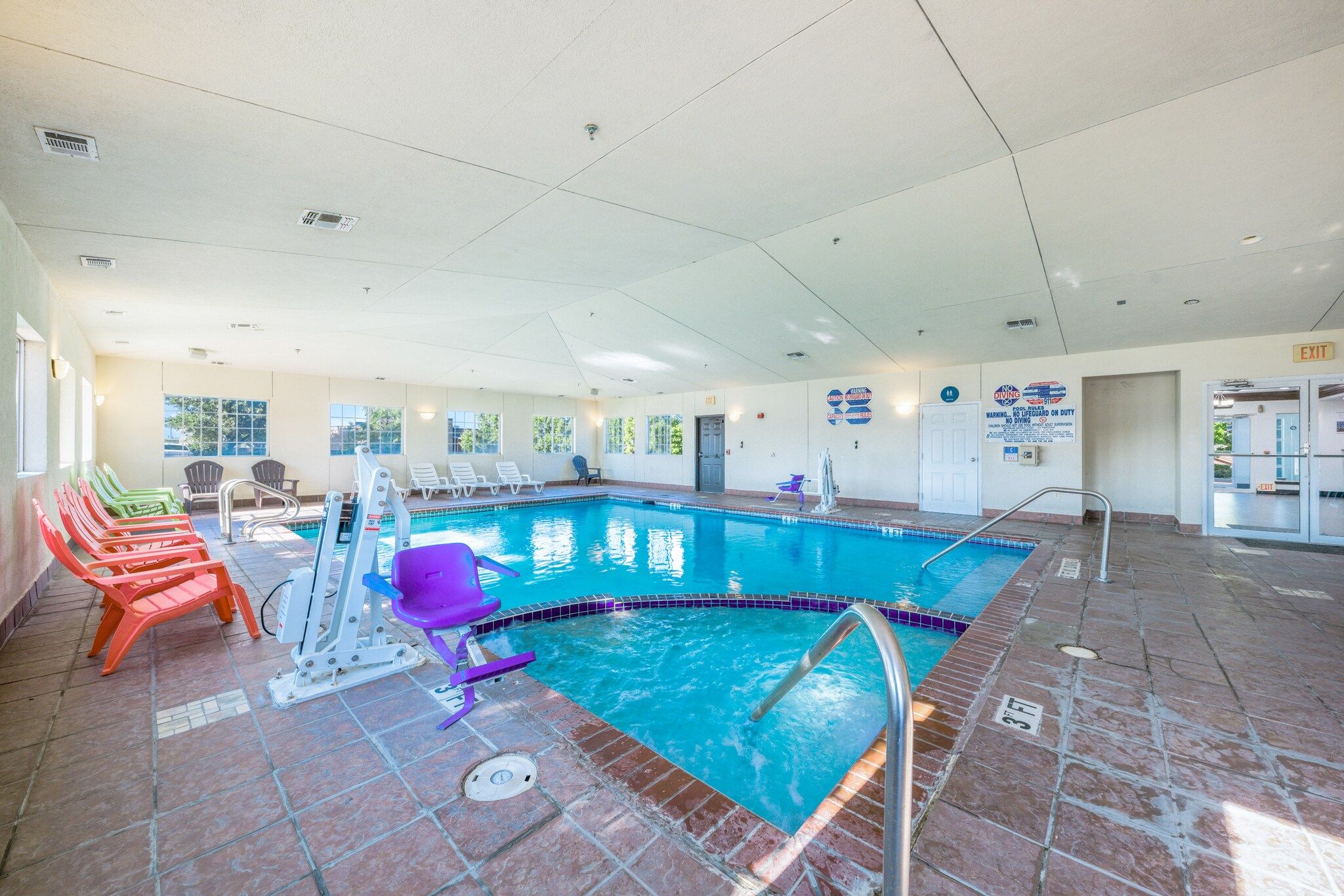 An indoor swimming pool with a diving board, multiple lounge chairs, and a tiled floor.
