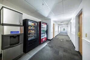 A hallway with vending machines and a refrigerator, carpeted floor, and doors on the right. - 2 King Beds | Suite, Non-Smoking (Decatur TX)