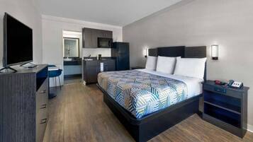 A modern hotel room with a bed, desk, and kitchenette.