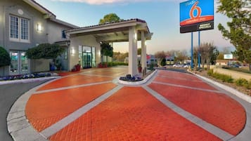 A hotel entrance with a covered walkway, a parking lot, and a billboard advertising weekly specials.