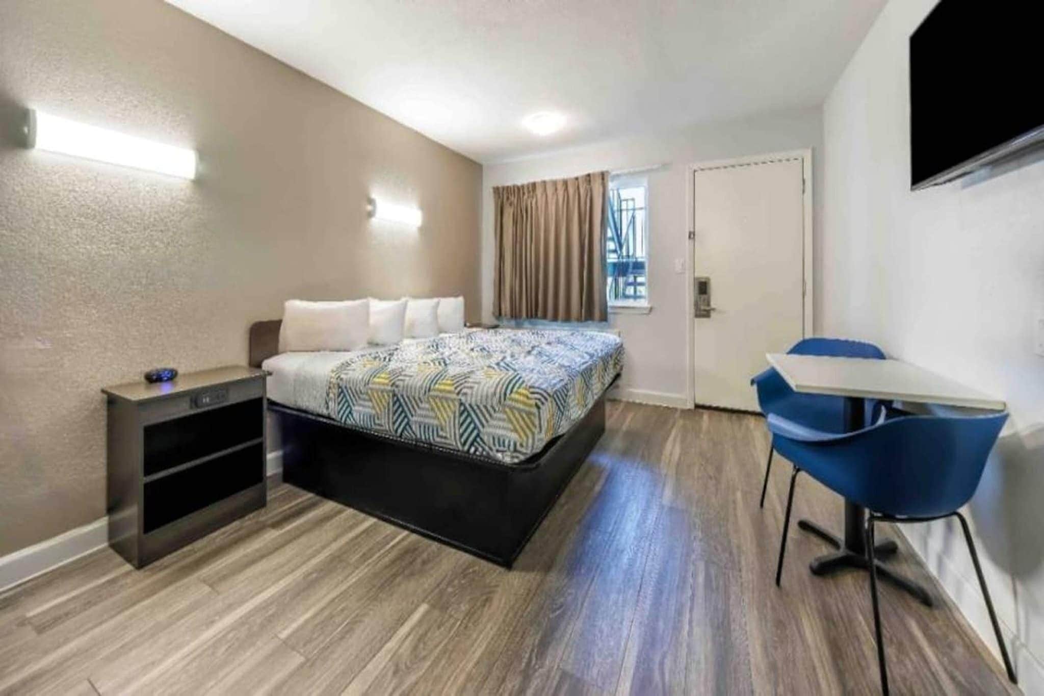 A hotel room with a bed, a desk, a chair, and a TV mounted on the wall.