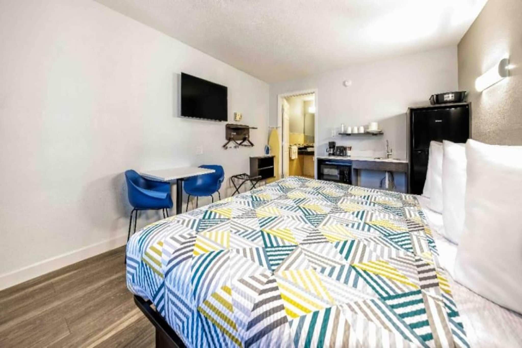 A hotel room with a bed, a desk, two chairs, a television, a kitchenette, and a bathroom.