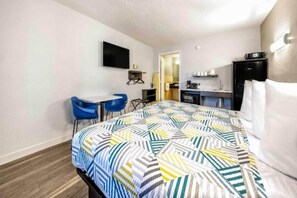 A hotel room with a bed, a desk, two chairs, a television, a kitchenette, and a bathroom. - 1 King Bed | Smoking (Fort Worth)
