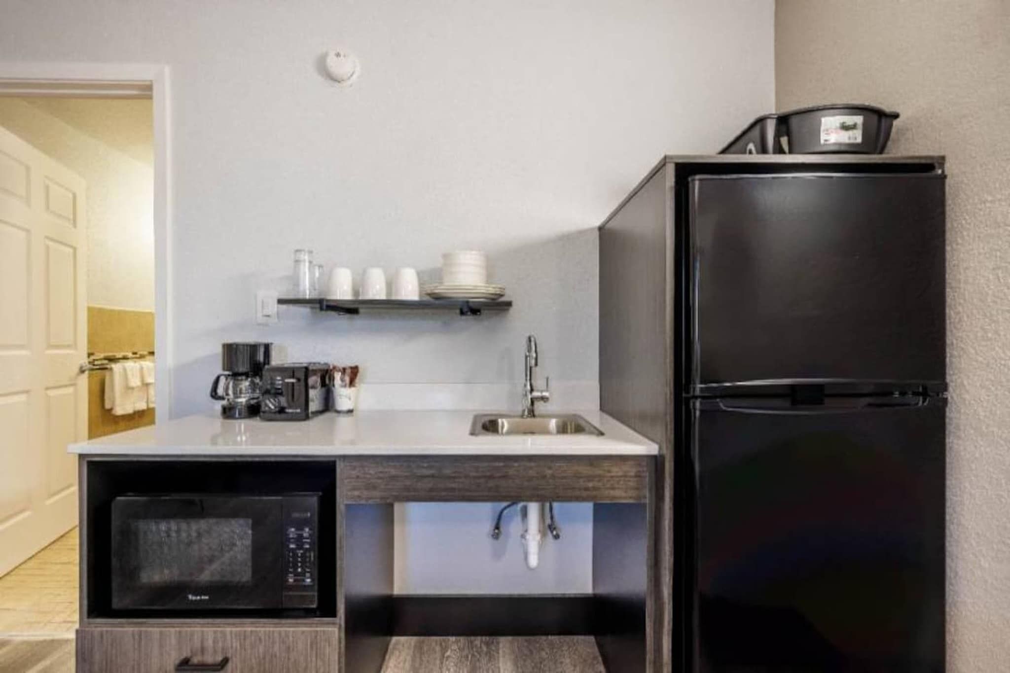 A compact kitchenette with a microwave, sink, and black refrigerator.
