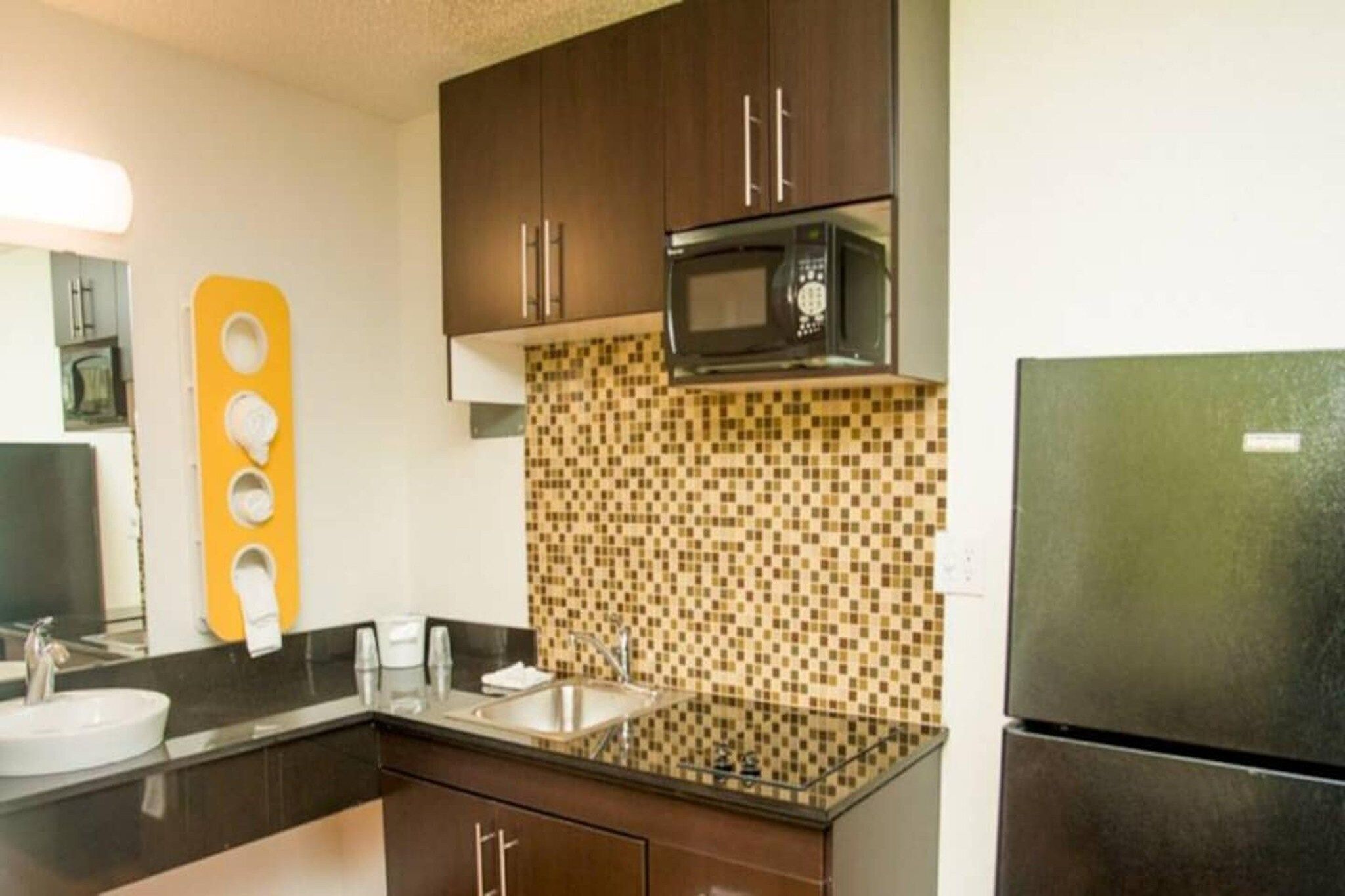 A compact kitchen with dark cabinets, a microwave, a sink, and a refrigerator.