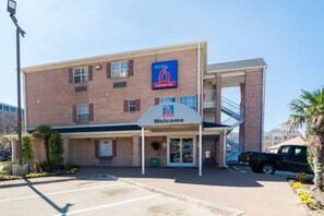 A 6 extended stay hotel with a 'Welcome' sign, a covered entrance, and a parking lot. - 1 King Bed | Smoking, Kitchen (Plano)