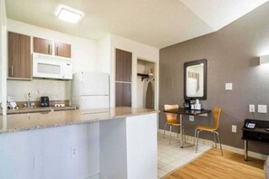 A compact kitchen with a microwave, refrigerator, and a dining area with chairs and a table. - 1 King Bed | Smoking, Kitchen (Plano)