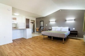A bedroom with a bed, bedside tables, a desk, and a kitchenette. - 1 King Bed | Smoking, Kitchen (Plano)