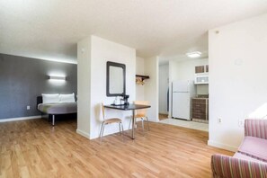 A modern apartment with a wooden floor, a dining area with a table and chairs, a kitchenette, a bed, and a striped sofa. - 1 King Bed | Smoking, Kitchen (Plano)