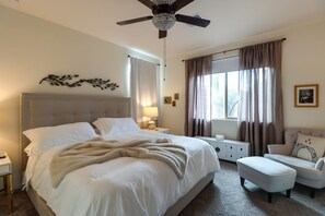 A hotel room with a bed, a nightstand, a lamp, a chair, a window with curtains, and a ceiling fan. - Tucson Desert Escape Near Outdoor Adventures (Tucson)