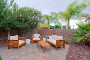 Ein Terrassenbereich im Freien mit Holzmöbeln, darunter Sofas und ein Couchtisch, umgeben von Pflanzen und einer Ziegelmauer.
