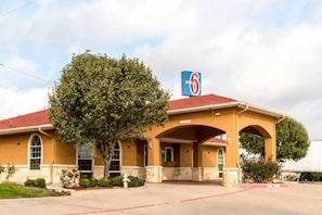 Ein Motel mit rotem Dach, ein großer Baum davor und ein Schild mit der Nummer sechs.