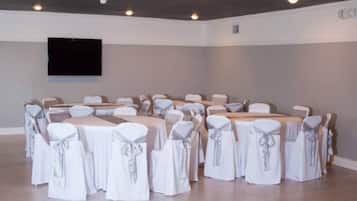 A conference room with tables and chairs, a flat-screen TV mounted on the wall, and a neutral color scheme.