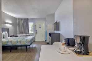Ein Hotelzimmer mit einem Bett, einem Schreibtisch mit Kaffeemaschine, einem Fernseher und einer Tür.