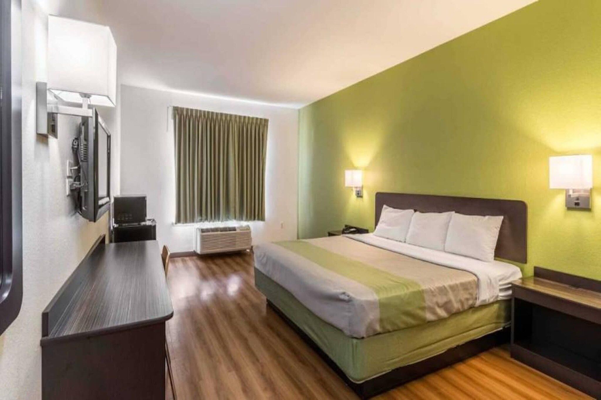 A hotel room with a bed, bedside table, lamp, and a window with curtains.