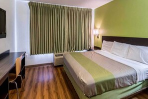 Ein Hotelzimmer mit Bett, Schreibtisch, Stuhl, einem Fenster mit Vorhängen und einer Wand-Klimaanlage.