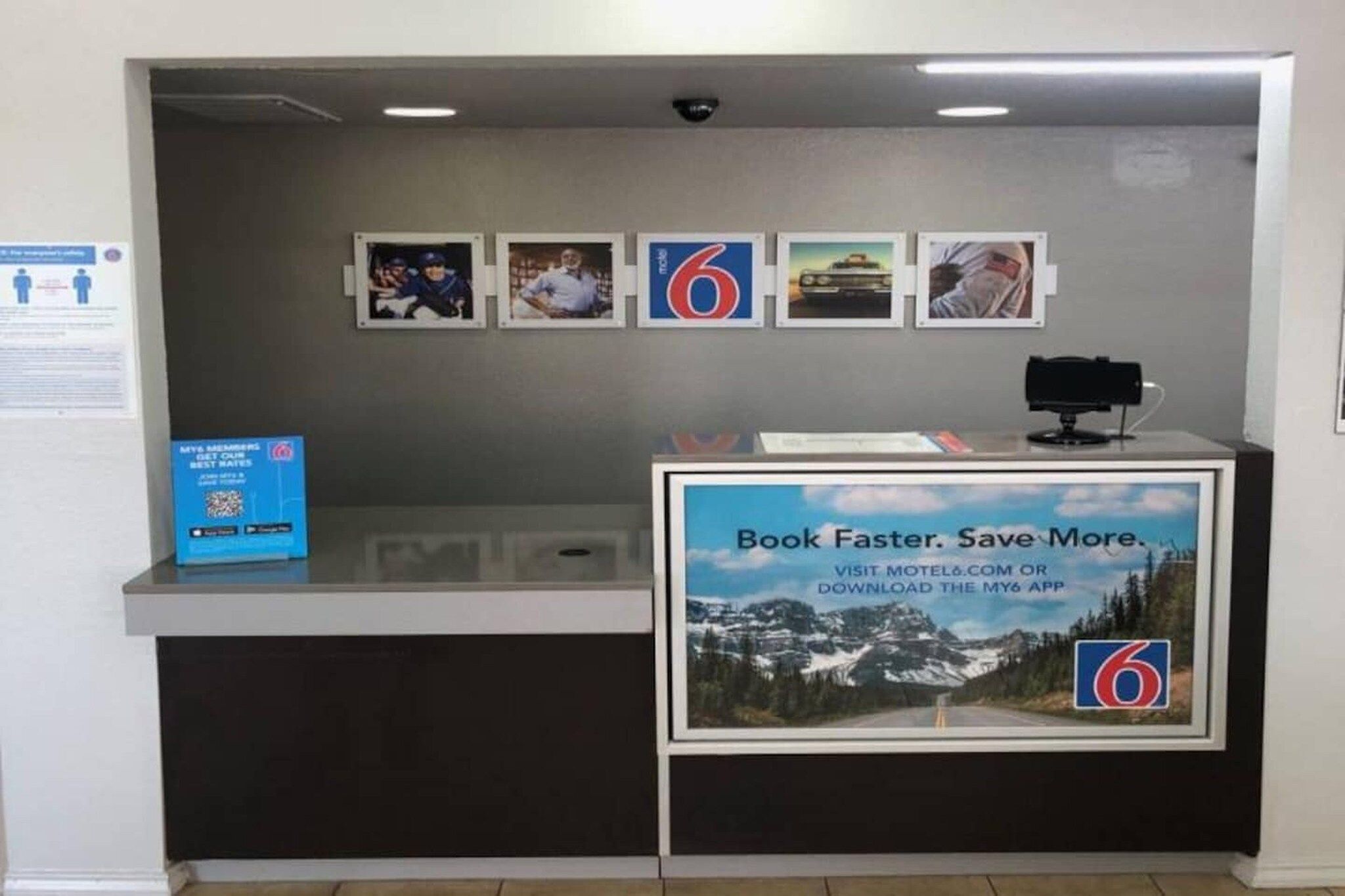 A reception desk with a sign promoting a mobile app, framed pictures on the wall, and a QR code for membership.