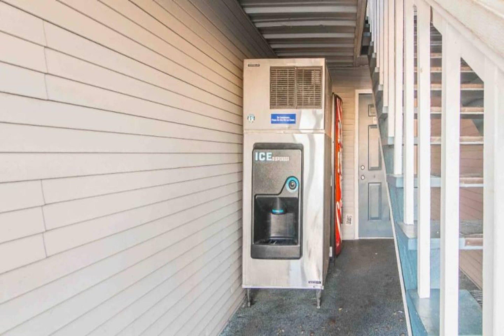 An ice dispenser outside a building with a metal roof and a brick wall.