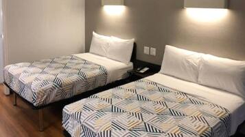 Two twin beds with patterned bedding, a bedside table with a phone, and wall-mounted lighting.