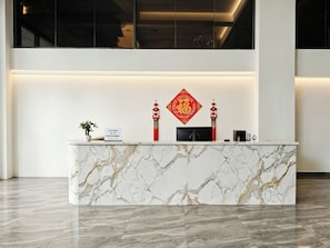 Un mostrador de recepción con encimera de mármol, una planta en maceta y decoraciones tradicionales rojas.