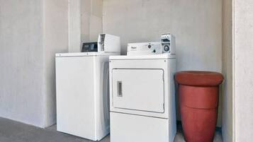 A laundry area with two white washing machines and a red trash bin.