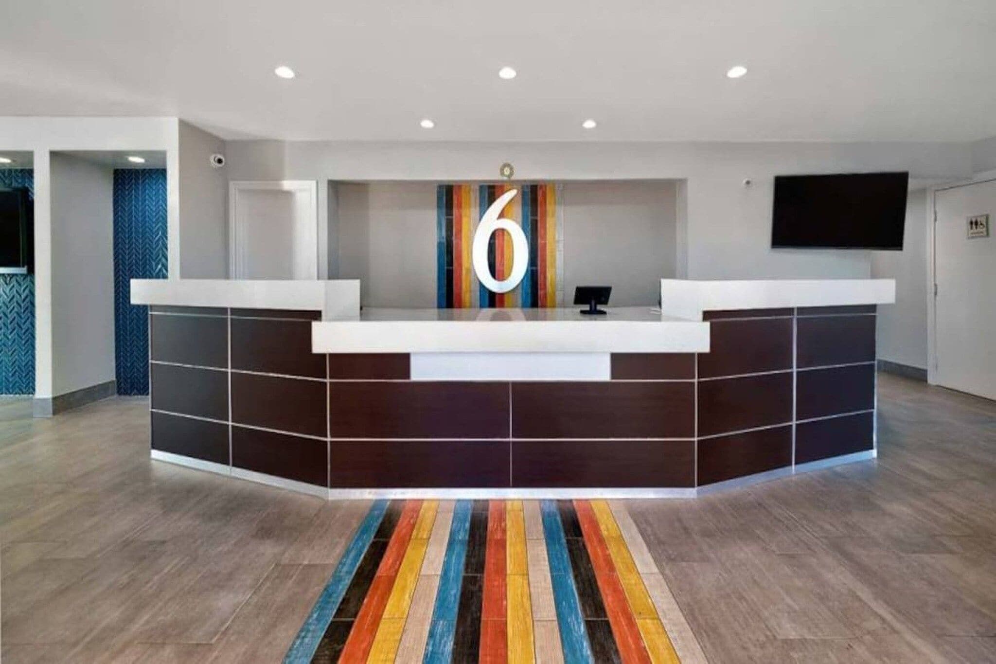 A reception desk with a large number '6' sign, a flat-screen TV, and a colorful striped carpet.
