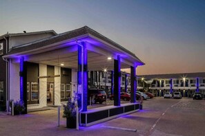 Un motel con un'area di parcheggio coperta e una fila di auto parcheggiate davanti.