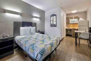 A hotel room with a bed, bedside tables, a desk, and a kitchenette. - 1 Queen Bed | Suite, Non-Smoking (Dallas)