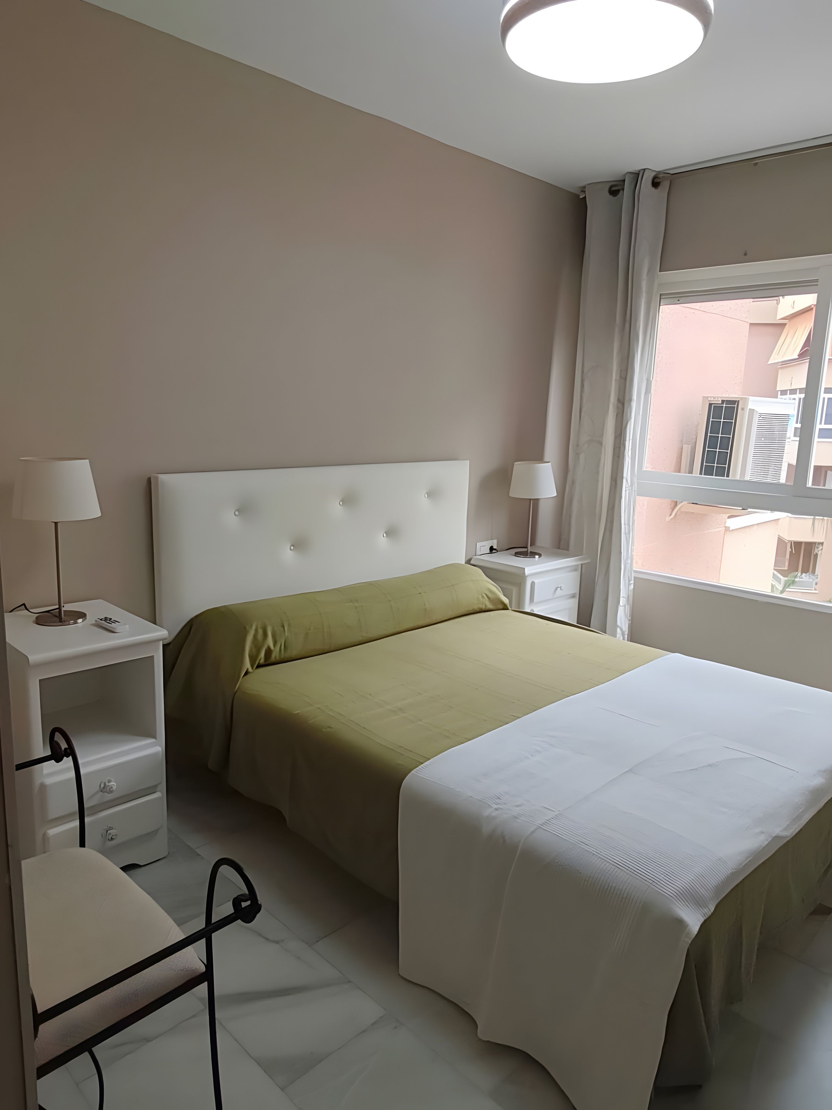 Een hotelkamer met een bed, nachtkastjes, lampen en een raam met uitzicht op gebouwen.