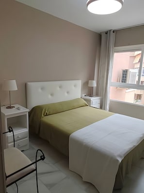 Een hotelkamer met een bed, nachtkastjes, lampen en een raam met uitzicht op gebouwen.