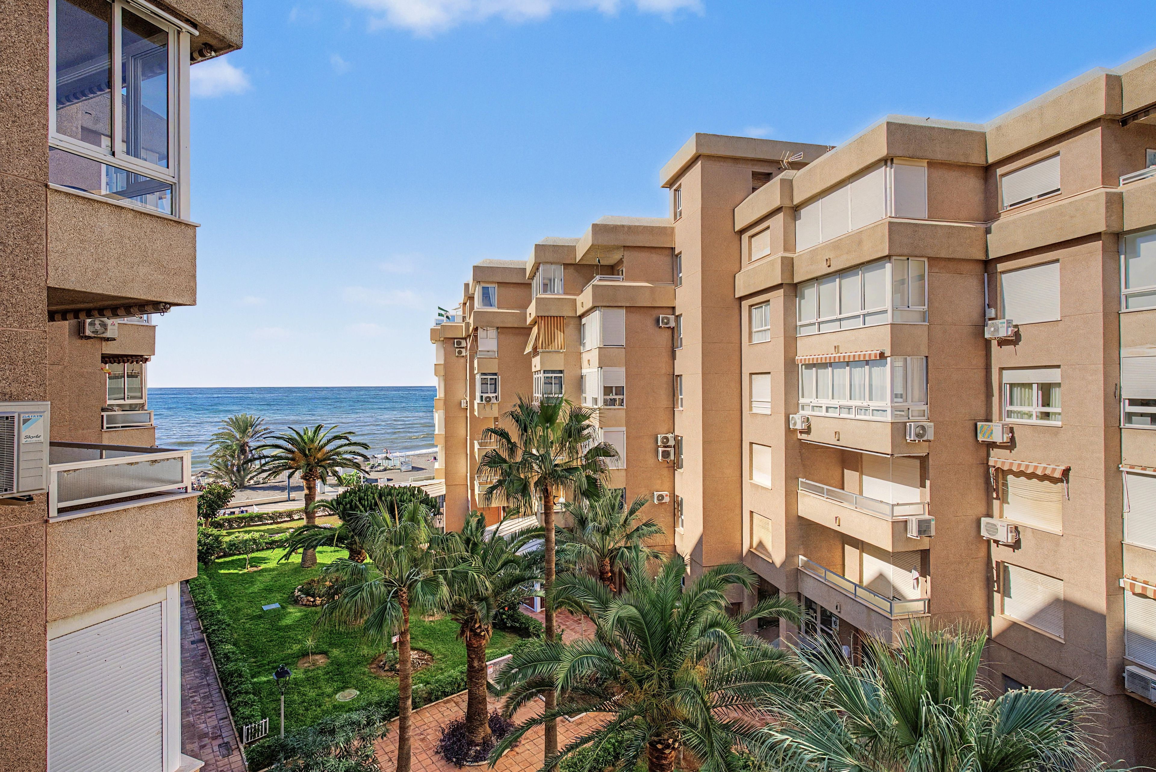 A multi-story hotel with balconies overlooking a beach and a landscaped courtyard with palm trees.
