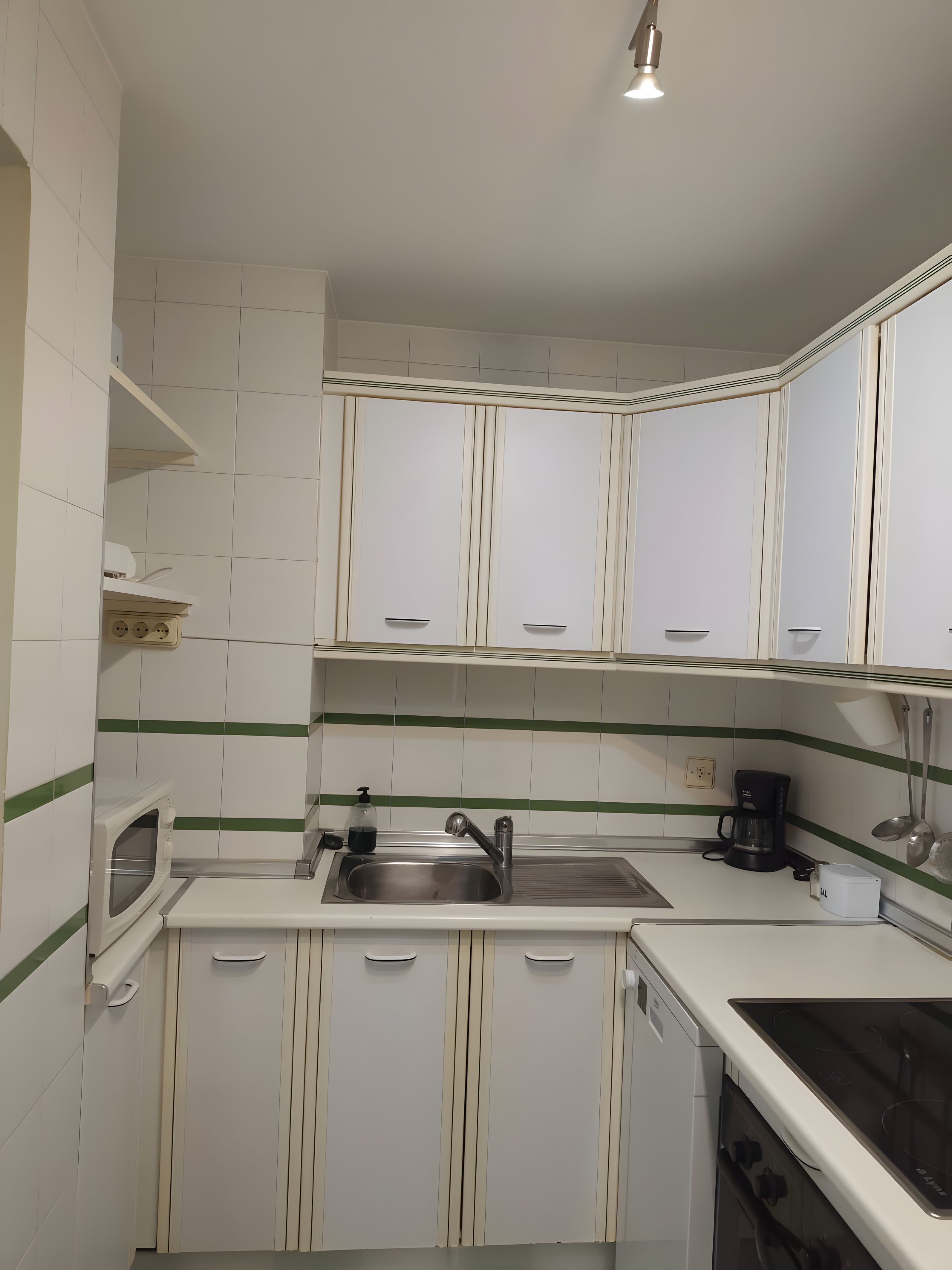 Een kleine keuken met witte kastjes, een roestvrijstalen spoelbak, een koffiezetapparaat en een ingebouwde oven.