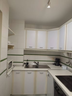 Een kleine keuken met witte kastjes, een roestvrijstalen spoelbak, een koffiezetapparaat en een ingebouwde oven.