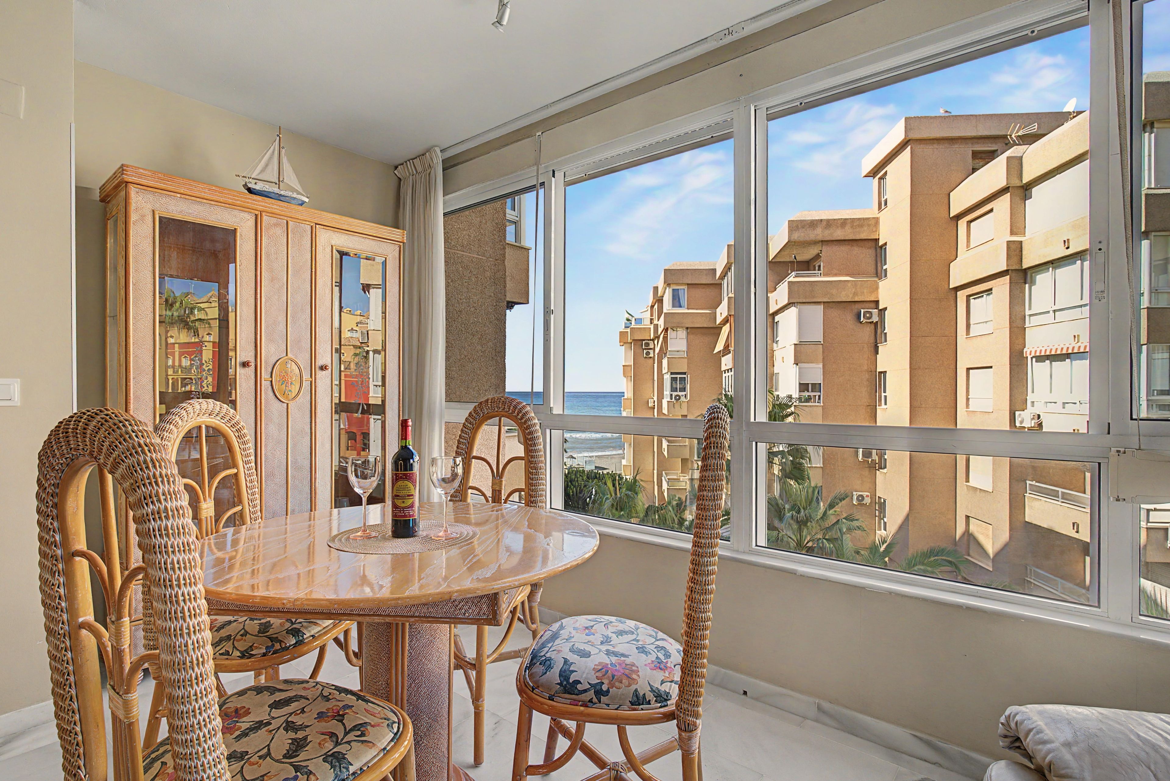 A spacious balcony with a view of a coastal building, furnished with wicker chairs and a marble table.
