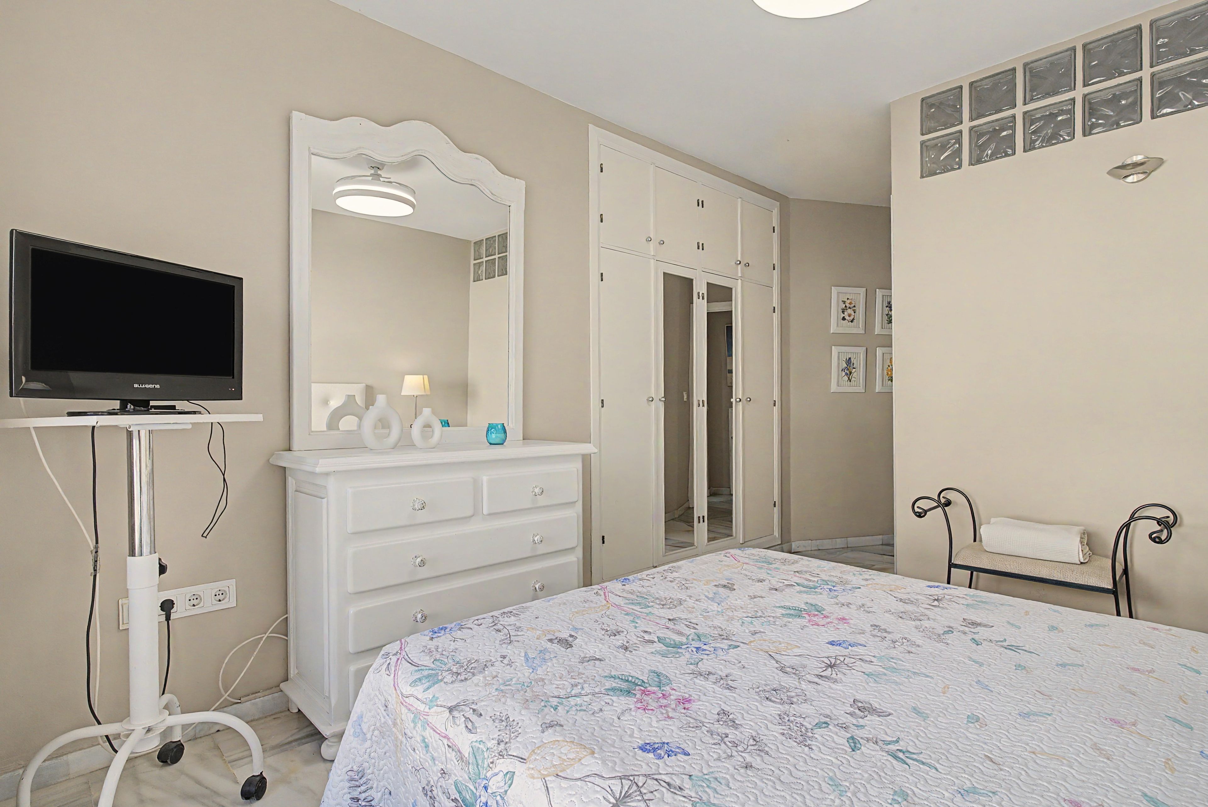 A bedroom with a bed, a TV, a dresser, a mirror, a wardrobe, and a bathroom with a towel rack.