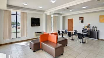 A hotel lobby with a seating area, a TV mounted on the wall, and a counter with amenities.