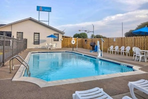 A swimming pool with a wooden fence, a building with a 'Welcome' sign, and outdoor seating.