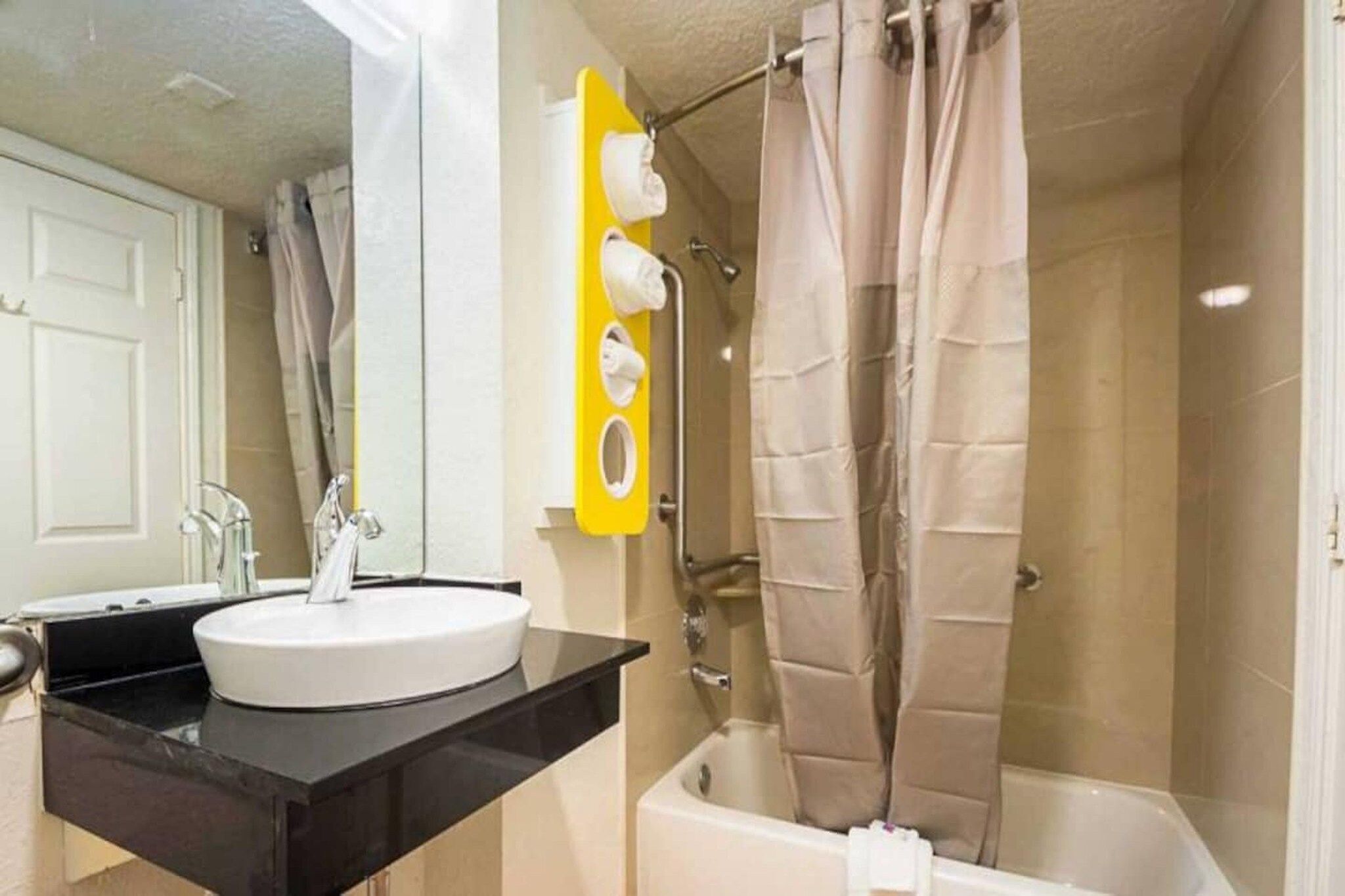 A bathroom with a white sink, a black countertop, a yellow towel rack, and a shower curtain.