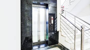 Un ascensor moderno con pantalla digital, piso de mármol y escalera con barandillas de metal.