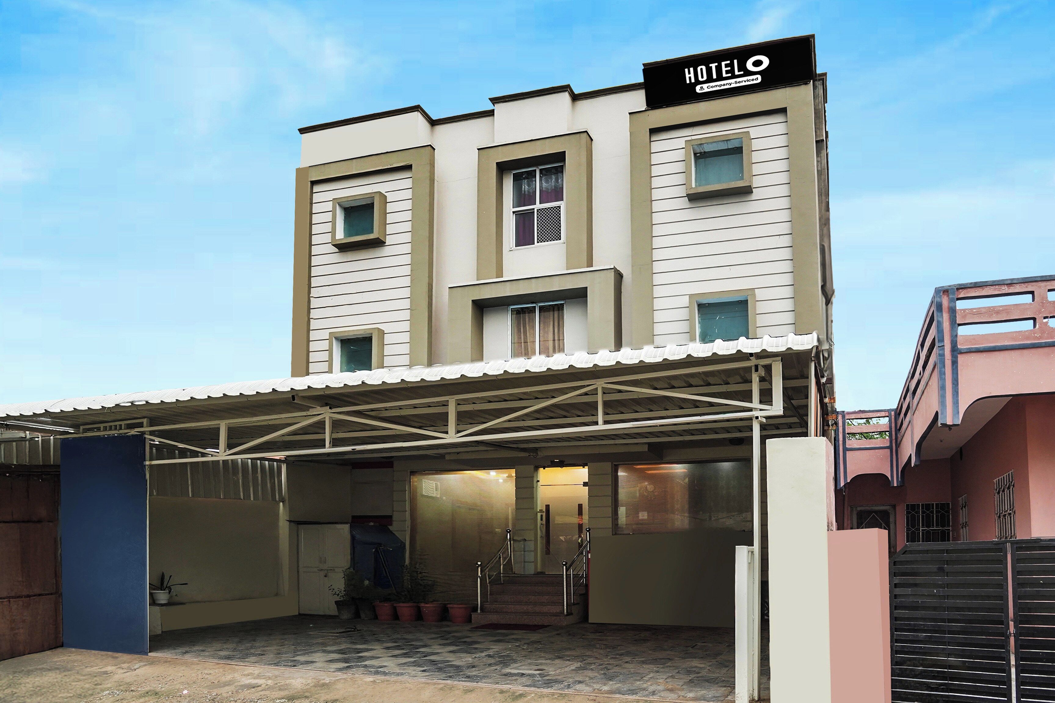 A hotel with a covered parking area, a staircase leading to the entrance, and a sign indicating it is a company-serviced hotel.