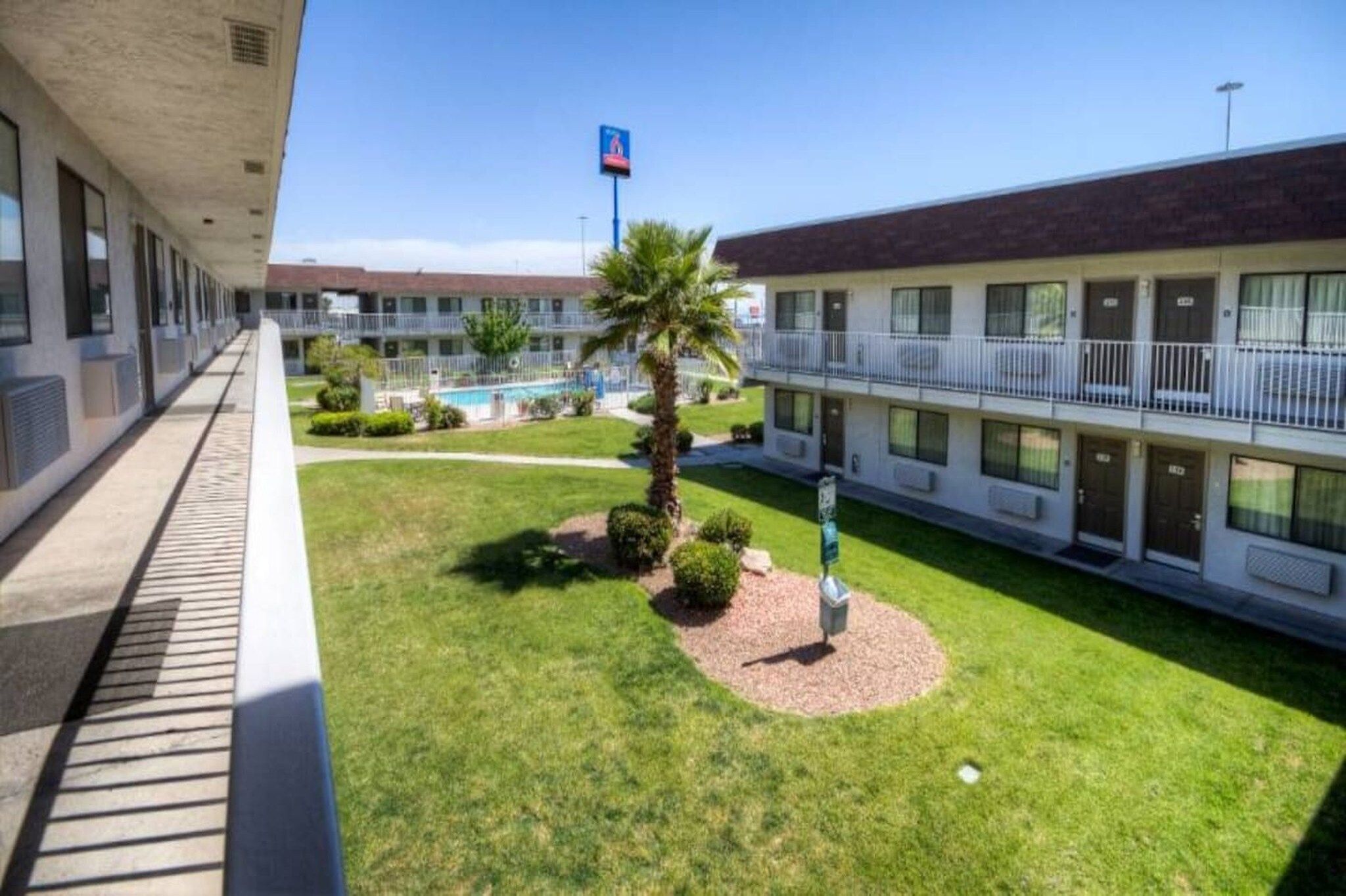 Un motel con piscina, una palma e cielo sereno.