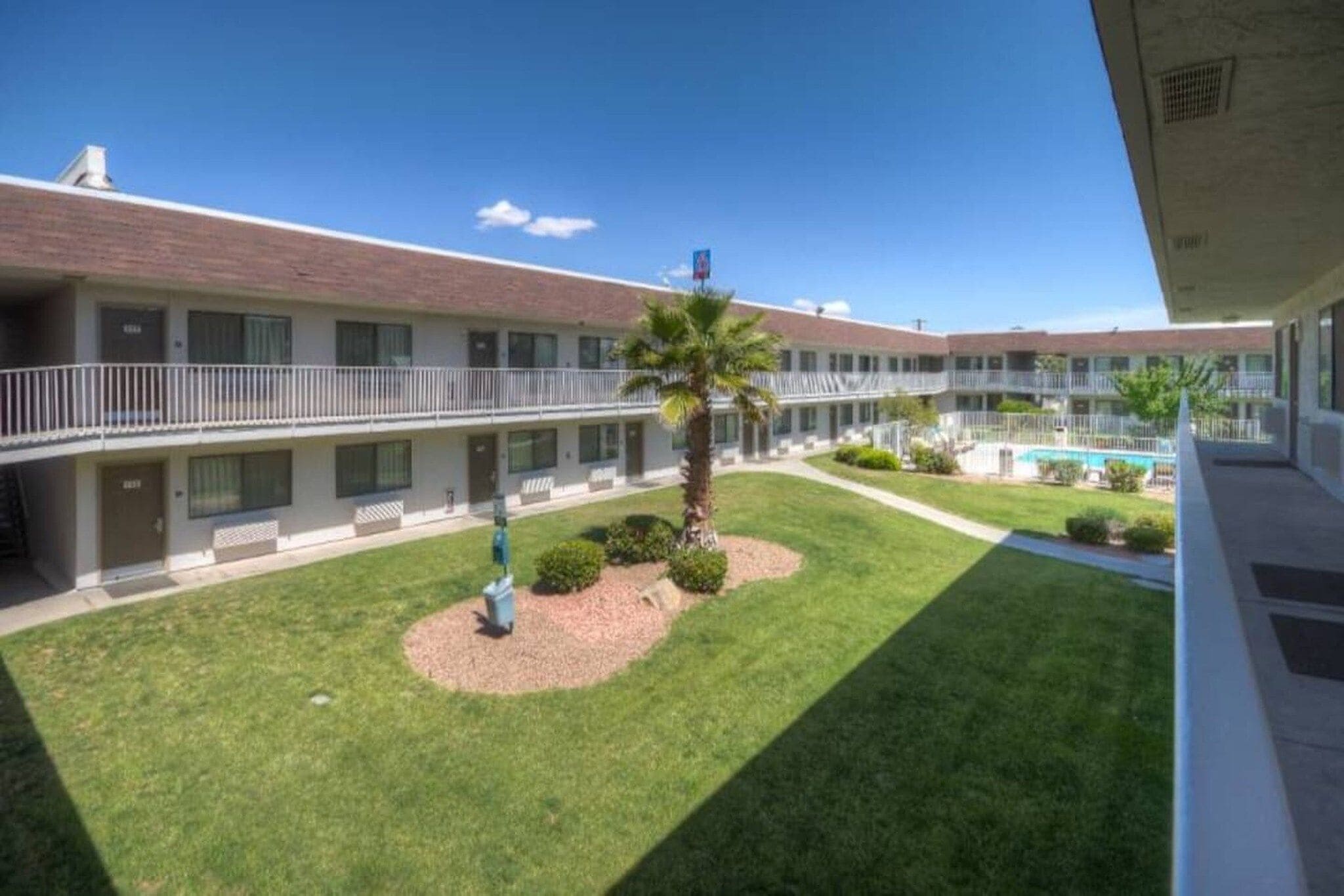 Un motel de varios pisos con un patio central que cuenta con una palmera, una pequeña piscina y un césped bien cuidado.