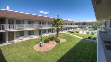 Un motel de varios pisos con un patio central que cuenta con una palmera, una pequeña piscina y un césped bien cuidado.