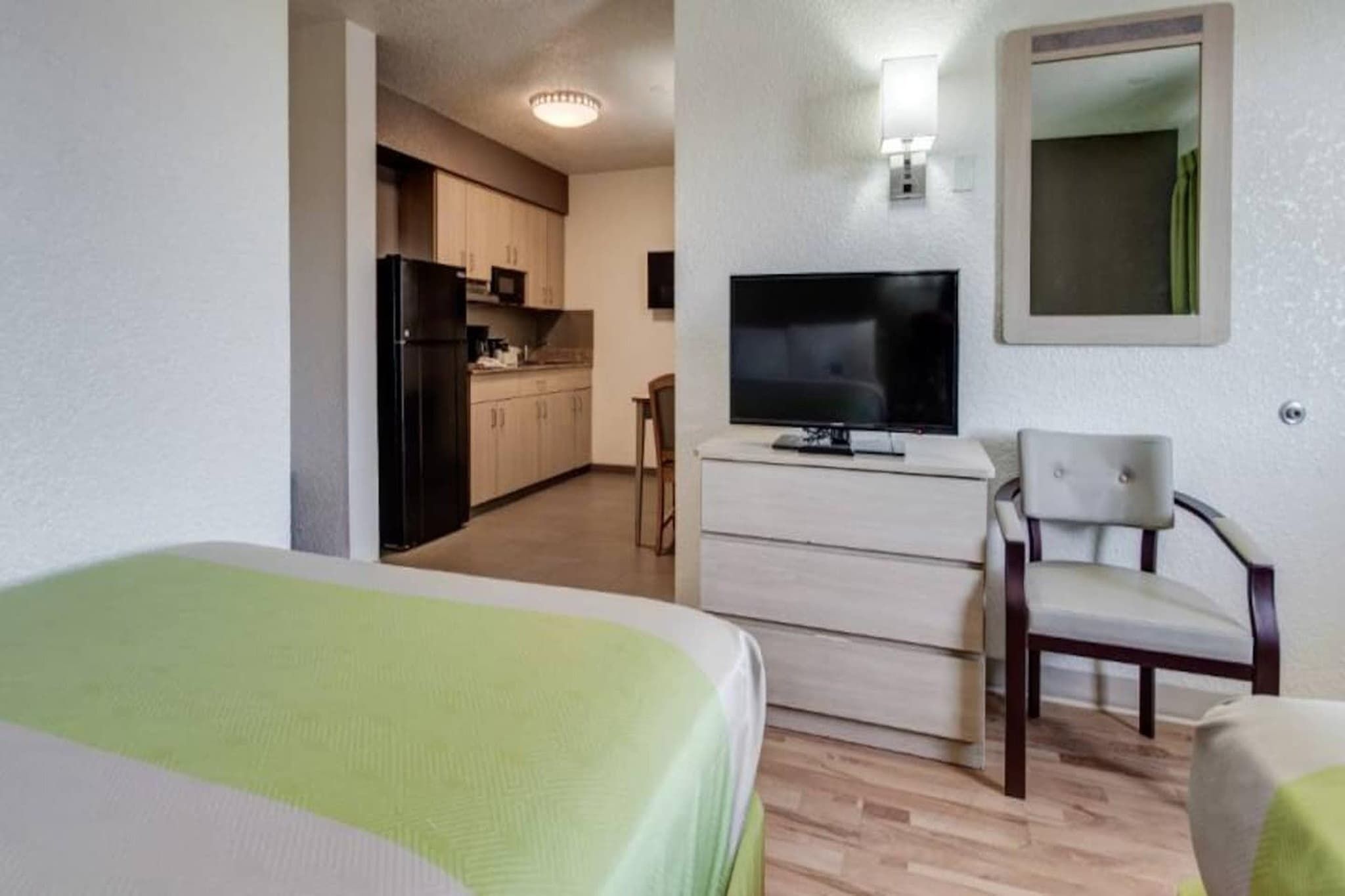 A hotel room with a bed, a TV, a chair, and a kitchenette.