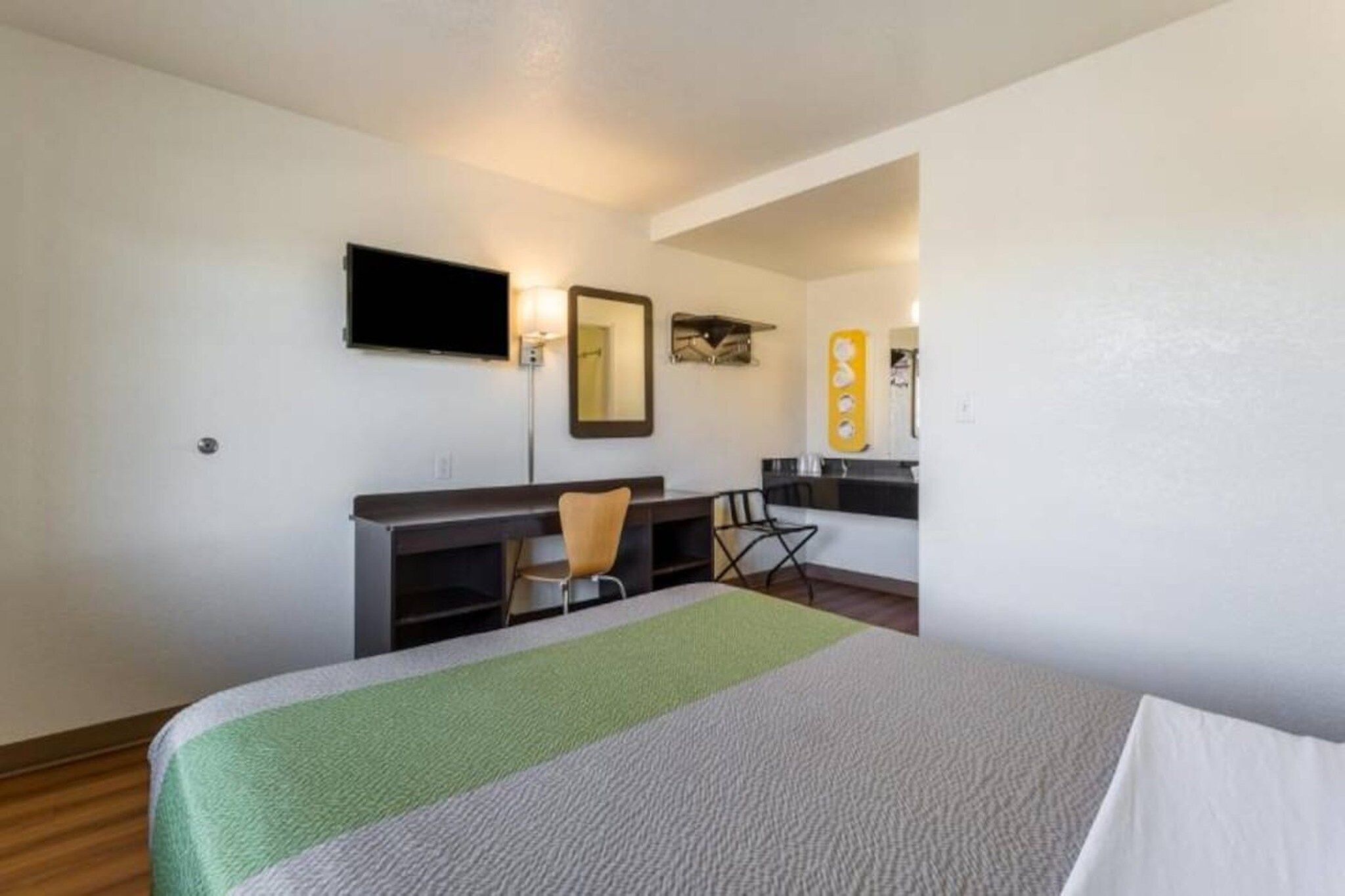 Una camera d'albergo con un letto, una scrivania, una sedia, una televisione e uno specchio.
