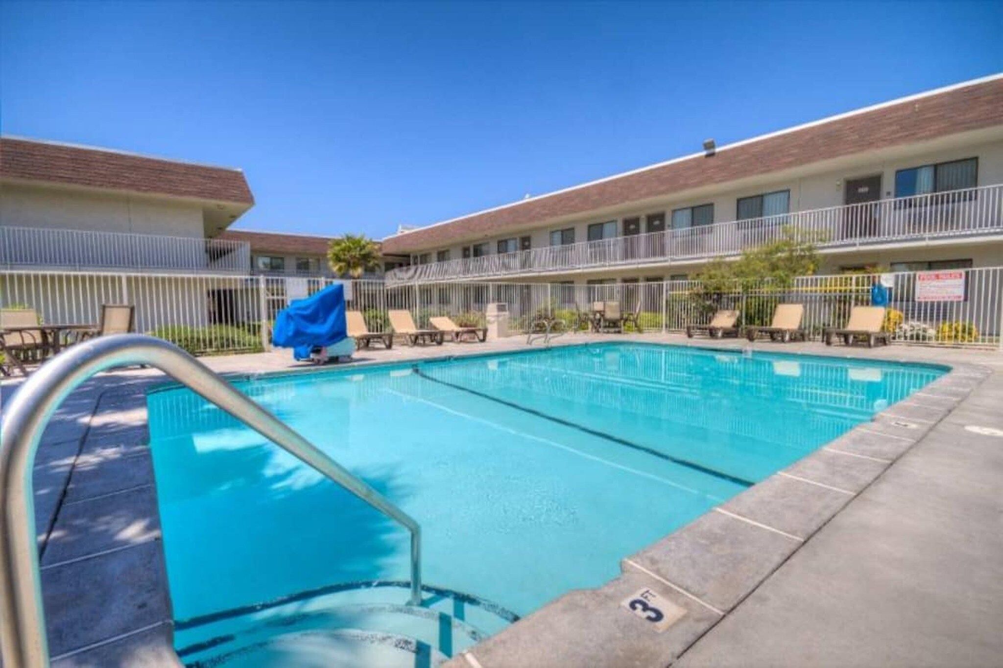 Une piscine dotée de chaises longues et d’un espace abrité, le tout entouré d’un bâtiment avec un balcon.
