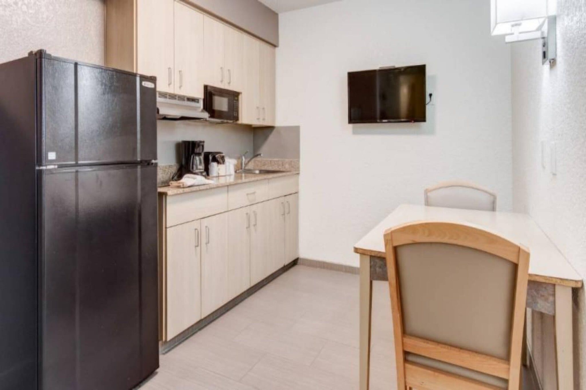 Cocina compacta con refrigerador, microondas y una pequeña mesa de comedor con una silla.