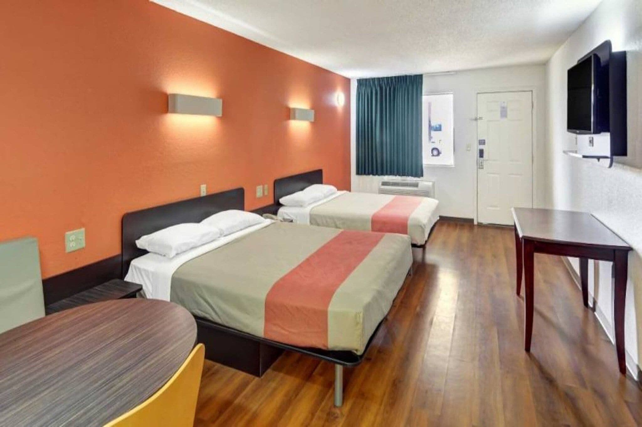Ein Hotelzimmer mit zwei Betten, einem Schreibtisch, einem Sessel und einem Fernseher.