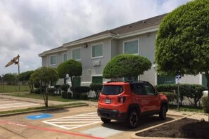 A parking lot with a red SUV, a crosswalk, and a building with a flat roof and multiple windows. - 1 King Bed | Non-Smoking, Kitchen (Burleson)